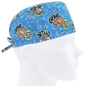 Op de afbeelding: Blauwe chirurgische scrub-muts met een witte rand en een herhalend patroon van botten, sterren en de tekst "ORTHO" en "Always time for a joint!"