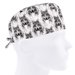 May include: A white surgical scrub cap featuring a repeating pattern of black and gray wolf faces and feathers. The cap has a tie closure at the back and is designed to be worn in a medical or veterinary setting.