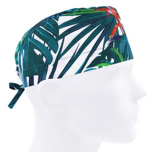 May include: A tropical-themed scrub cap featuring a vibrant pattern of green palm leaves and red flowers against a white background. The cap is tied at the back with a matching fabric tie. The cap is designed to be worn in a medical or professional setting.