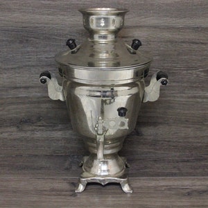 May include: A silver samovar with black handles and a spout. The samovar is a traditional Russian tea kettle.