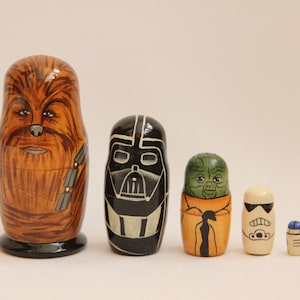 Può includere: Set di sei bambole russe a tema Star Wars. La bambola più grande è Chewbacca, seguita da Darth Vader, Yoda, uno Stormtrooper e un piccolo droide blu e bianco.