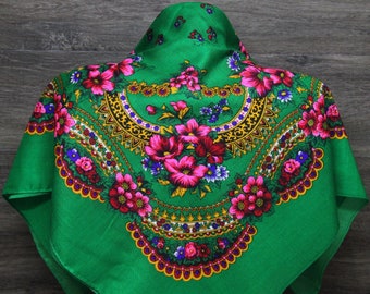 May include: A green headscarf with a floral pattern. The pattern features pink, red, yellow, and blue flowers. The scarf has a gold and purple trim.