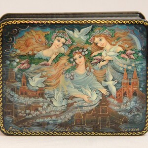Puede incluir: Una caja de madera con una escena pintada de tres mujeres con el pelo suelto y palomas blancas volando a su alrededor. Las mujeres llevan coronas de flores y están rodeadas de una ciudad. La caja está decorada con un borde dorado.