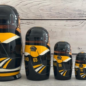 May include: Set of five nesting dolls, each painted with a black, yellow, and white hockey jersey design. The largest doll has the number 37, and the smallest has the number 40. The dolls are arranged in size order.