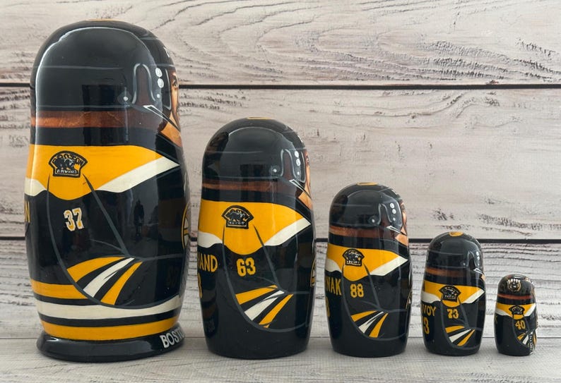 May include: Set of five nesting dolls, each painted with a black, yellow, and white hockey jersey design. The largest doll has the number 37, and the smallest has the number 40. The dolls are arranged in size order.