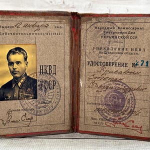 May include: An open vintage identification document with red edges, featuring a black and white portrait of a person in uniform on the left side. The document contains Cyrillic text, official stamps, handwritten signatures, and the number 714.