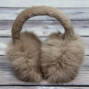 May include: Taupe-coloured earmuffs with a fluffy, fur-like texture. The headband is also covered in the same soft material. These earmuffs are designed to keep ears warm in cold weather.