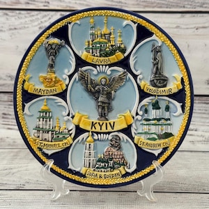 Puede incluir: Plato decorativo de cerámica con monumentos de Kiev, Ucrania. El plato es azul marino con ribetes dorados e incluye imágenes de Maydan, Lavra, St. Michael Ch., Kyiv, Sofia & Bogdan, Volodimir y St. Andrew Ch.