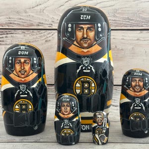 May include: A set of six nesting dolls, each painted with a hockey player in a black, yellow, and white uniform. The dolls feature the team's logo and player numbers. The largest doll is about 7 inches tall.