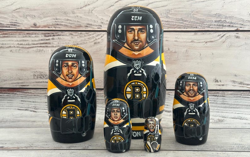 May include: A set of six nesting dolls, each painted with a hockey player in a black, yellow, and white uniform. The dolls feature the team's logo and player numbers. The largest doll is about 7 inches tall.