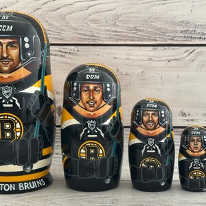 May include: A set of five nesting dolls, each painted to resemble a hockey player in a black, yellow, and white uniform. The largest doll reads "BOSTON BRUINS" at the base. Each doll has a hockey helmet and the number 37, 69, 66, 72, and 75.