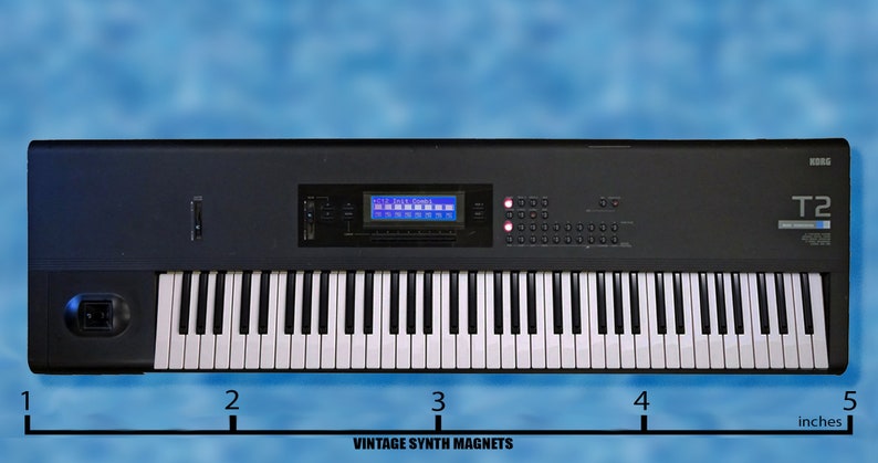 Peut inclure: Un clavier Korg T2 noir avec un clavier de 61 touches, un &eacute;cran LCD bleu et une vari&eacute;t&eacute; de boutons et de molettes. Le clavier mesure 12,7 cm de large.