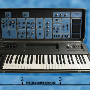 May include: A vintage black and silver synthesizer with a blue control panel and a 49-key keyboard. The synthesizer is open and the control panel is visible. The synthesizer is 3 inches wide.