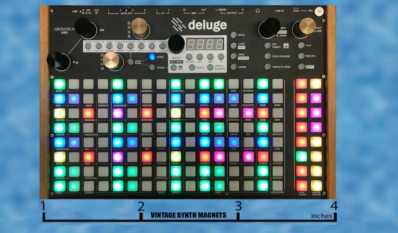 Puede incluir: Un sampler y secuenciador Deluge negro y plateado con una cuadr&iacute;cula de 64 pads de luces de colores. La pantalla muestra "88.88". El dispositivo tiene 10 cm de ancho.
