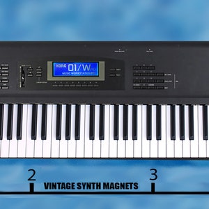 Peut inclure: Un clavier de synth&eacute;tiseur num&eacute;rique noir avec un &eacute;cran LCD bleu affichant "01/W" et le texte "Roland" et "DI/WFD" sur le devant. Le clavier mesure 10 cm de large.