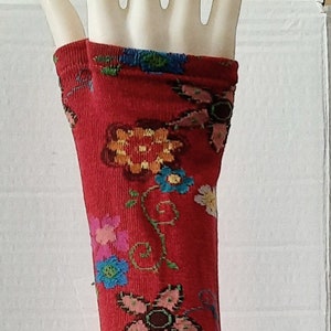Puede incluir: Calentadores de brazos rojos con un patrón floral. El patrón floral incluye flores rosas, azules, amarillas y marrones. Los calentadores de brazos tienen una banda marrón en la parte inferior con un diseño floral.