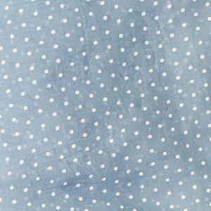 May include: A light blue fabric featuring a repeating pattern of small, solid white polka dots. The material has a subtle, slightly mottled texture with variations in the blue tone, creating a soft, consistent appearance across the surface.