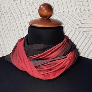 May include: A red and black ombre infinity scarf made of soft fabric. The scarf is draped around a mannequin's neck.