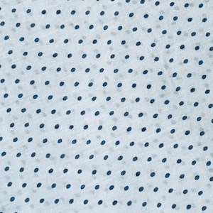May include: A light blue fabric featuring a repeating pattern of small, dark navy blue polka dots. The material has a visible, slightly textured weave, creating a consistent and uniform dotted design across the entire surface of the textile.