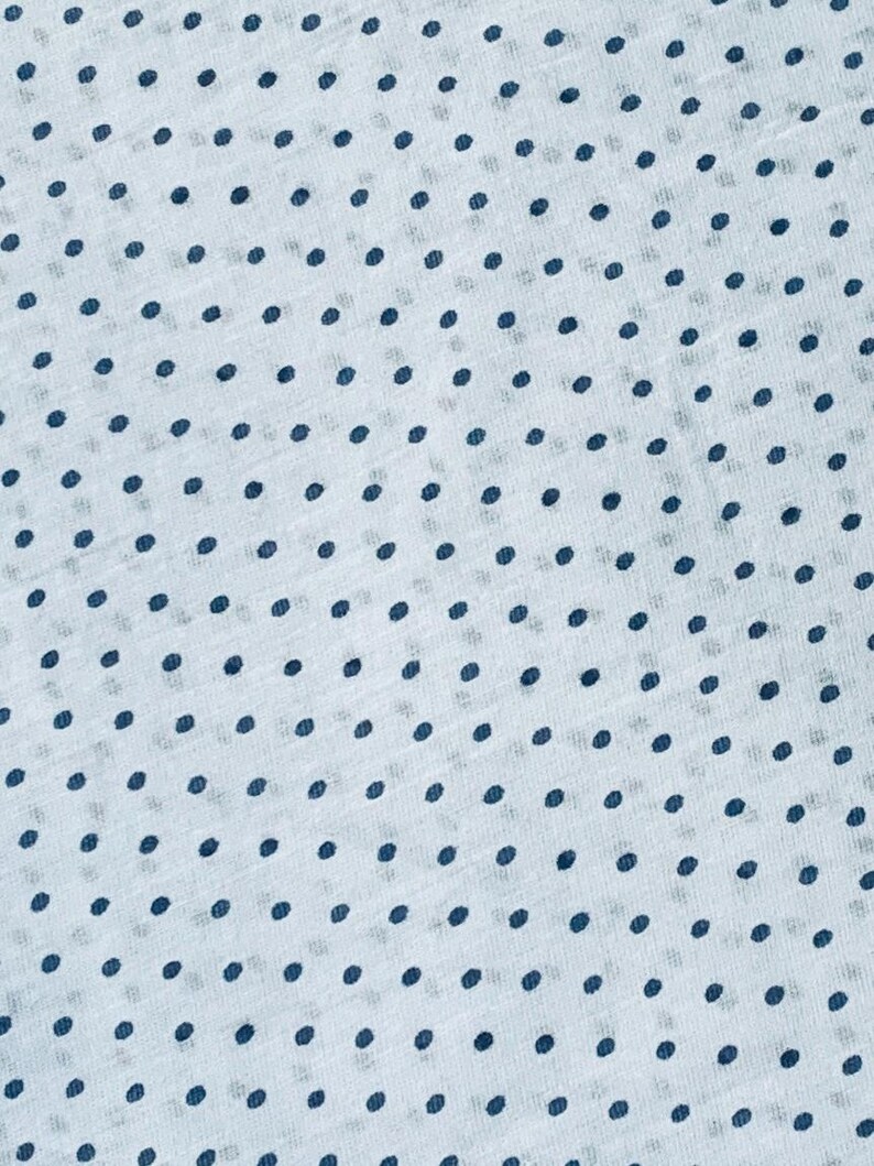May include: A light blue fabric featuring a repeating pattern of small, dark navy blue polka dots. The material has a visible, slightly textured weave, creating a consistent and uniform dotted design across the entire surface of the textile.