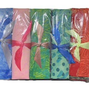 Könnte beinhalten: Ein Set aus fünf rechteckigen Stoffbündeln, die in Klarsichtfolie verpackt und jeweils mit einem Satinband zusammengebunden sind. Die Stoffe zeigen verschiedene Farben wie Blau, Rosa, Grün, Türkis und Rot mit unterschiedlichen Mustern.