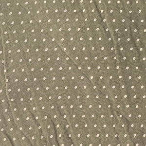 May include: A sage green fabric featuring a repeating pattern of small, white, circular polka dots. The material has a slightly textured, woven appearance with visible folds and creases running diagonally across the surface of the textile.
