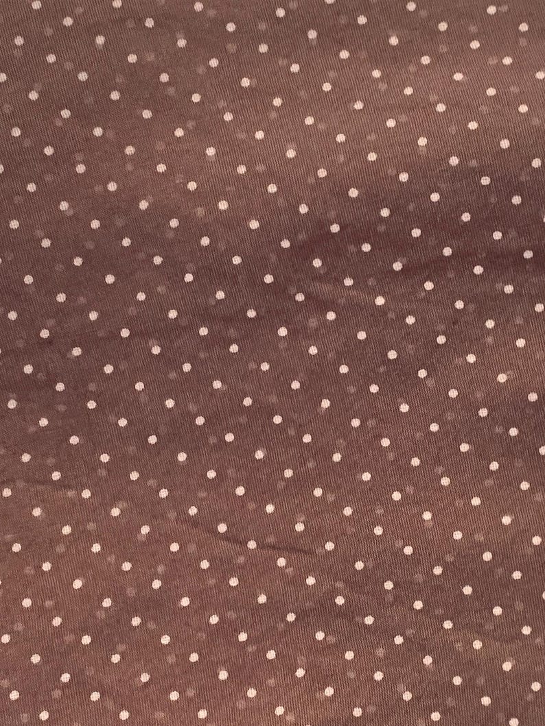 May include: A brown fabric featuring a repeating pattern of small, evenly spaced white polka dots. The material has a slightly sheer, lightweight texture with a consistent grid-like arrangement of the circular white spots across the surface.