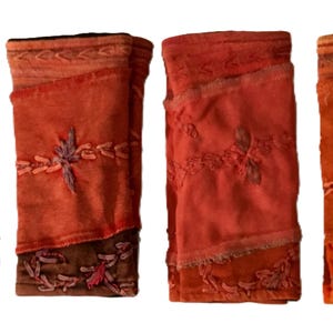Op de afbeelding: Vier geborduurde vierkante stoffen in tinten van bruin, oranje en rood. Elk vierkant heeft een ander bloemenmotief en is gemaakt van een patchwork van verschillende stoffen.