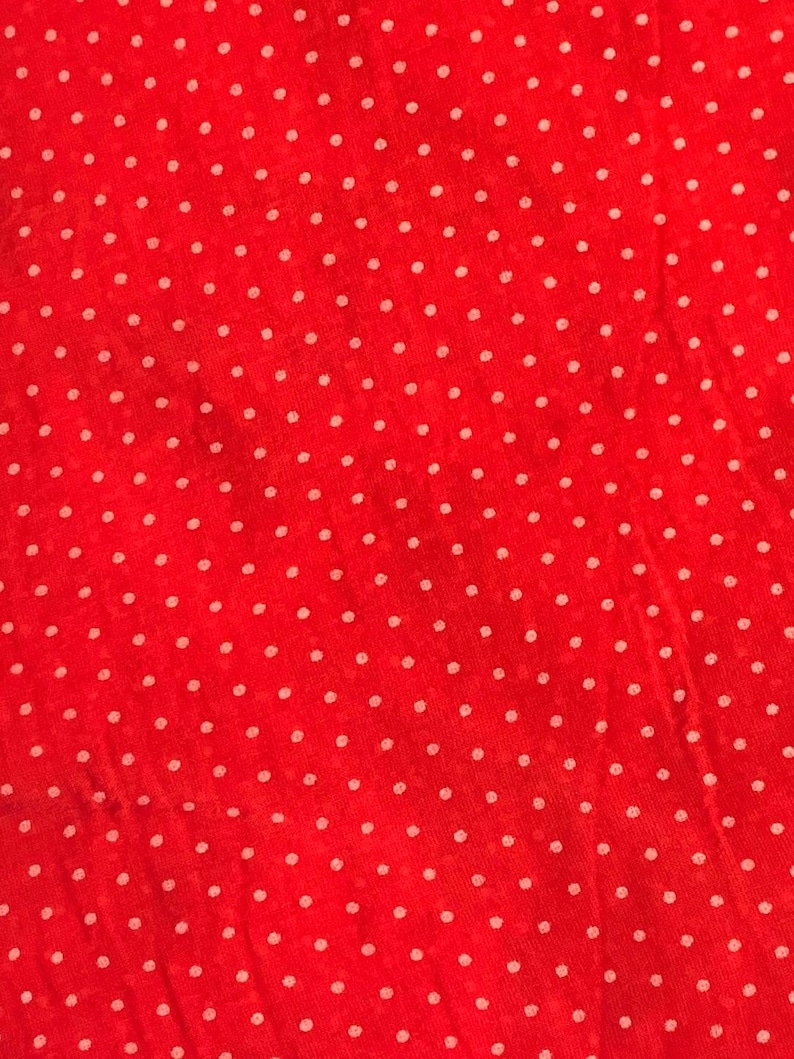 May include: A vibrant red fabric featuring a repeating pattern of small, evenly spaced white polka dots. The material has a slightly textured, semi-sheer appearance with visible weave details throughout the surface of the textile.