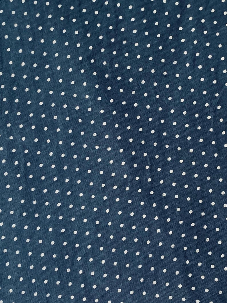 May include: A dark blue fabric featuring a repeating pattern of small, white, circular polka dots distributed evenly across the entire surface. The material has a visible, slightly textured weave, creating a consistent and uniform appearance.