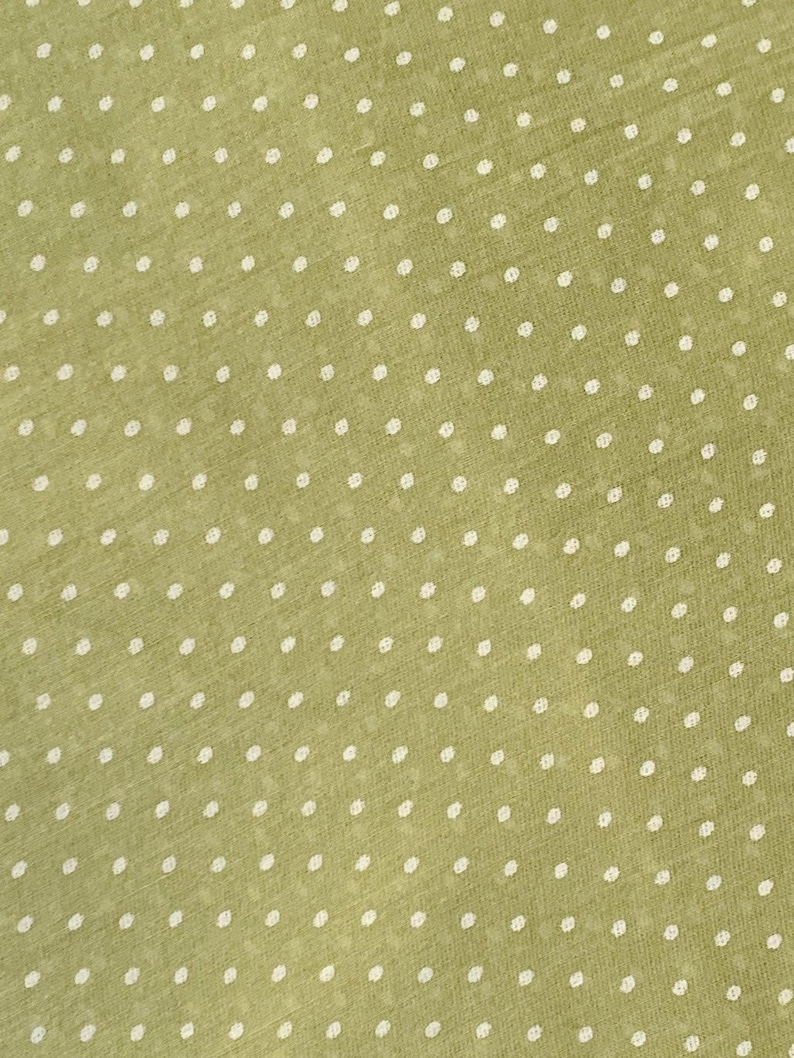 May include: A sage green fabric featuring a repeating pattern of small, white, circular polka dots. The material has a visible, fine-textured weave with a consistent, evenly spaced arrangement of dots across the entire surface of the textile.