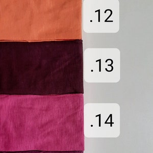 K&ouml;nnte beinhalten: F&uuml;nf Stoffmuster in verschiedenen Rot-, Orange-, Lila- und Rosat&ouml;nen. Die Muster sind mit den Nummern .11 bis .15 beschriftet.