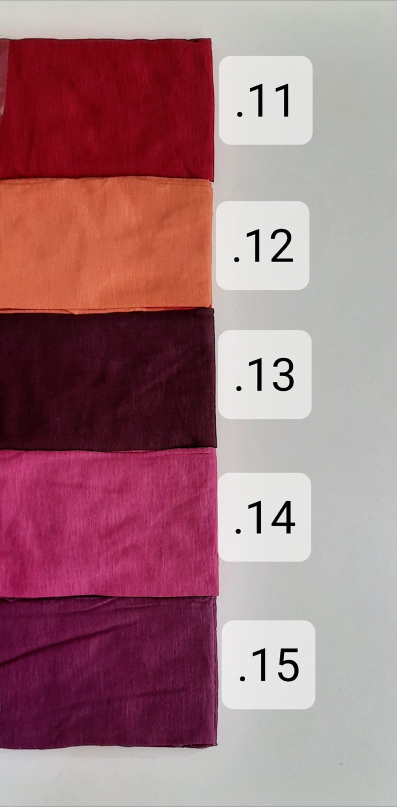 K&ouml;nnte beinhalten: F&uuml;nf Stoffmuster in verschiedenen Rot-, Orange-, Lila- und Rosat&ouml;nen. Die Muster sind mit den Nummern .11 bis .15 beschriftet.