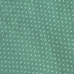 May include: A light green fabric featuring a repeating pattern of small, white, circular polka dots distributed evenly across the surface. The material has a slightly textured, semi-sheer appearance with subtle folds and creases throughout the textile.