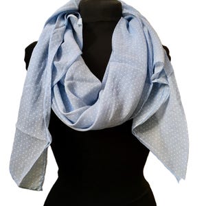 May include: A light blue scarf featuring a repeating pattern of small white polka dots. The scarf is draped in soft folds, showcasing its lightweight fabric and consistent color palette throughout the entire piece, creating a simple and classic look.
