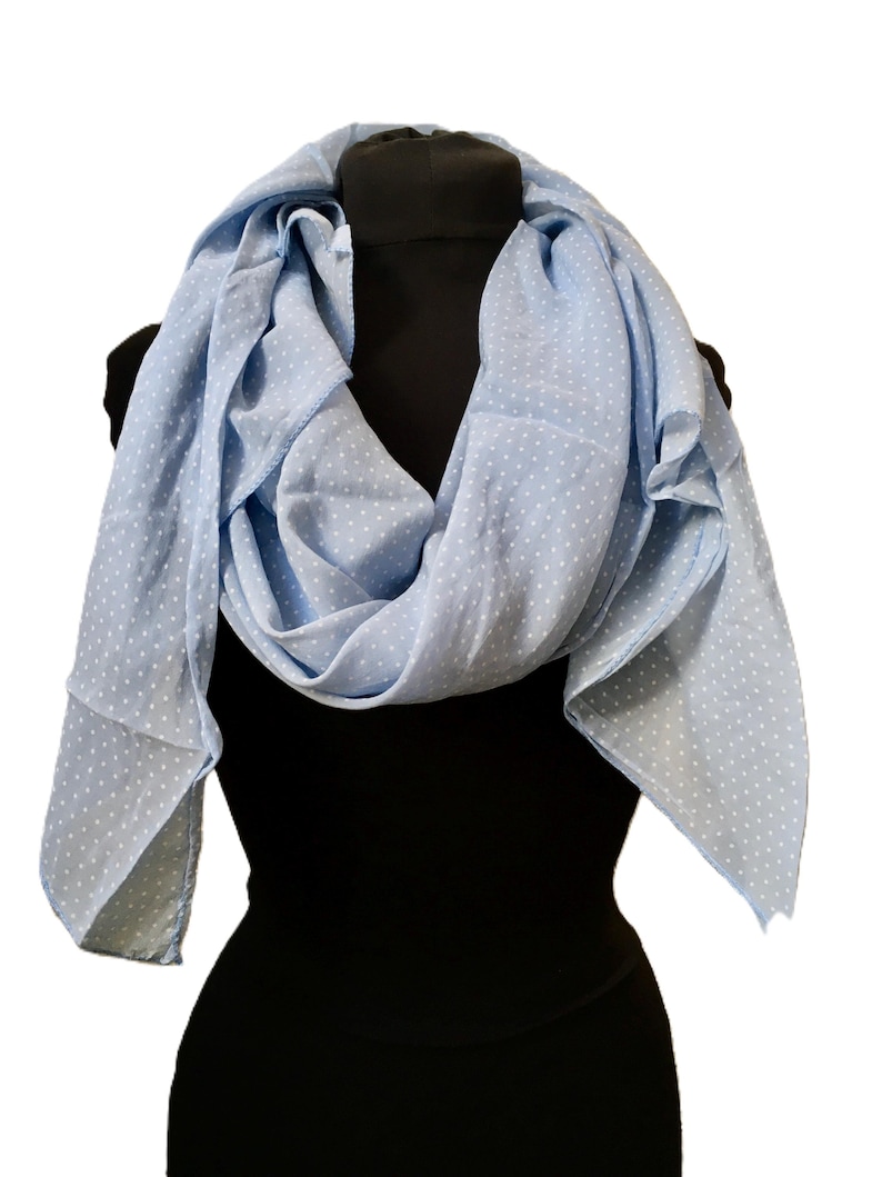 May include: A light blue scarf featuring a repeating pattern of small white polka dots. The scarf is draped in soft folds, showcasing its lightweight fabric and consistent color palette throughout the entire piece, creating a simple and classic look.