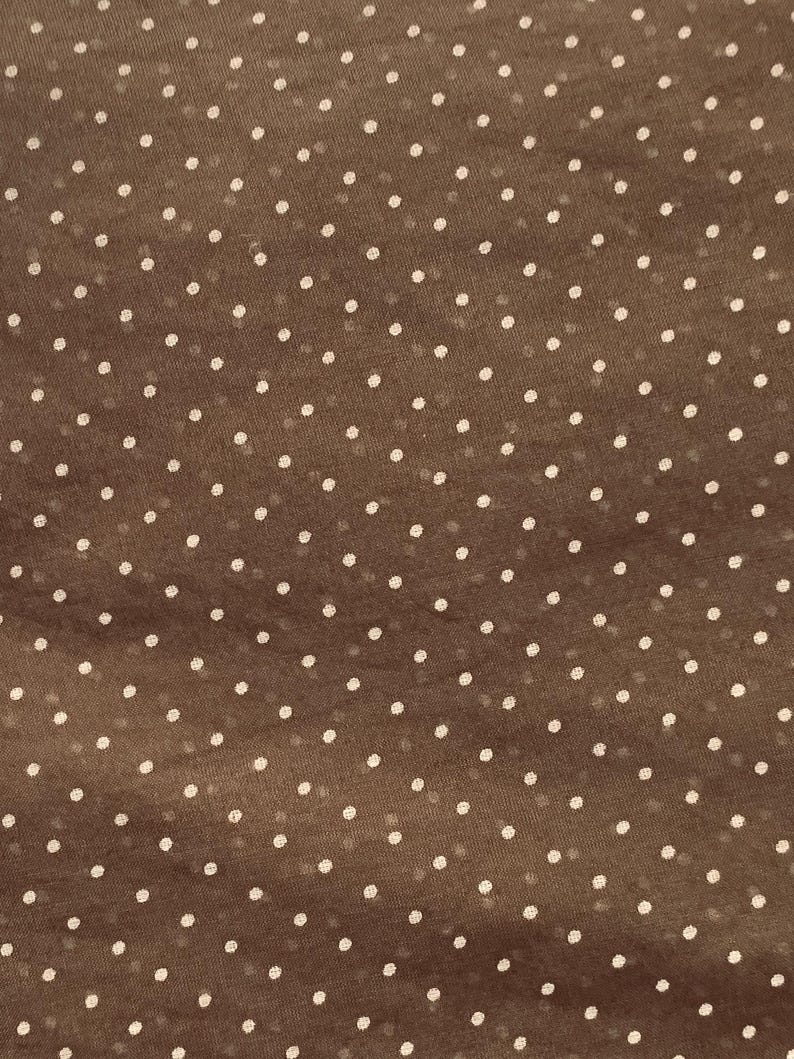 May include: A brown fabric featuring a repeating pattern of small, evenly spaced white polka dots. The material has a slightly translucent quality, showing a consistent texture across the surface with a simple, classic geometric design.