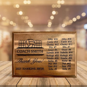 May include: A wooden plaque with a volleyball net and ball design. The text "COACH SMITH" is engraved on the plaque. The text "Thank You!" is engraved below the net and ball. The text "2023 HAWKINS HIGH" is engraved below the text "Thank You!" A list of names and numbers is engraved on the right side of the plaque.