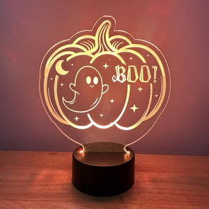 May include: A clear acrylic pumpkin-shaped night light with a ghost and the word "BOO!" etched into it. The light is on and illuminating the design.