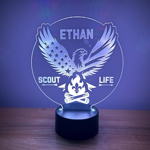 May include: A white acrylic night light with a design of an eagle with outstretched wings, a campfire, and the text "ETHAN SCOUT LIFE".