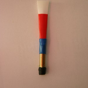 Puede incluir: Una caña de oboe de plástico blanca, roja y azul con una base de latón y una punta de goma negra.