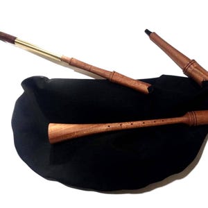 May include: A traditional bagpipe with a black bag and wooden components. The chanter, drones, and blowpipe are made of wood, with brass accents on the blowpipe. The bag is black, and the instrument is set against a white background.