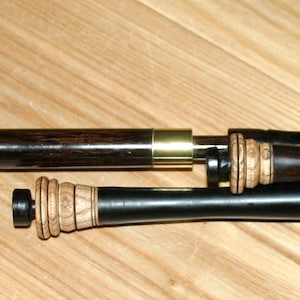 Può includere: Un set di cornamuse in legno nero con accenti dorati. Le cornamuse sono smontate e disposte su una superficie in legno.