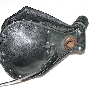 May include: Black leather mask with a rounded shape, metal studs, and a wooden accent. The mask has a strap and a fabric-covered tube. The design is reminiscent of historical plague doctor masks.