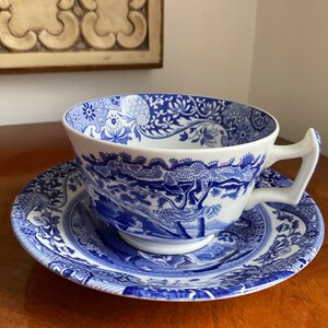 May include: A blue and white porcelain teacup and saucer set with a floral and landscape design.