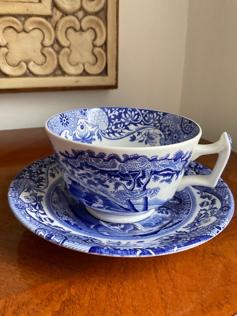 May include: A blue and white porcelain teacup and saucer set with a floral and landscape design.