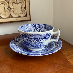 May include: A blue and white porcelain teacup and saucer set with a floral pattern. The cup has a handle and the saucer has a scalloped edge.