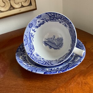 May include: A blue and white teacup and saucer set with a floral pattern. The saucer has a scalloped edge. The teacup has a handle and a scene of a building and trees in the centre.