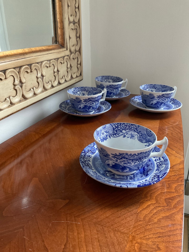 May include: Four blue and white teacups and saucers with a floral pattern. The cups and saucers are arranged on a wooden table.