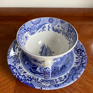 May include: A blue and white porcelain teacup and saucer set with a floral pattern. The cup and saucer feature a blue and white landscape scene with a castle.